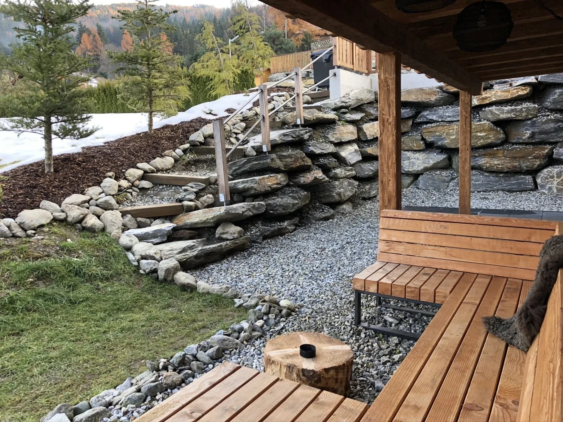 Holz-Loungebank im Garten mit Natursteinmauer