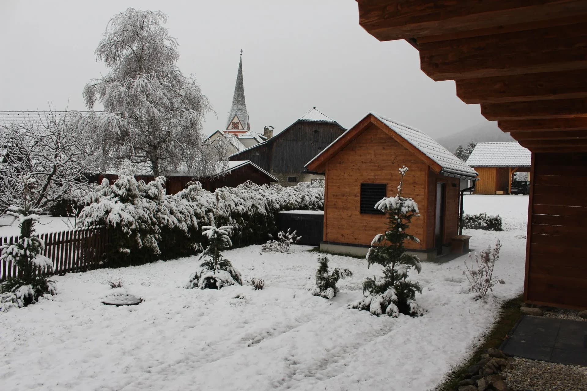 Verschneiter Garten mit Saunahaus und Dorfkirche