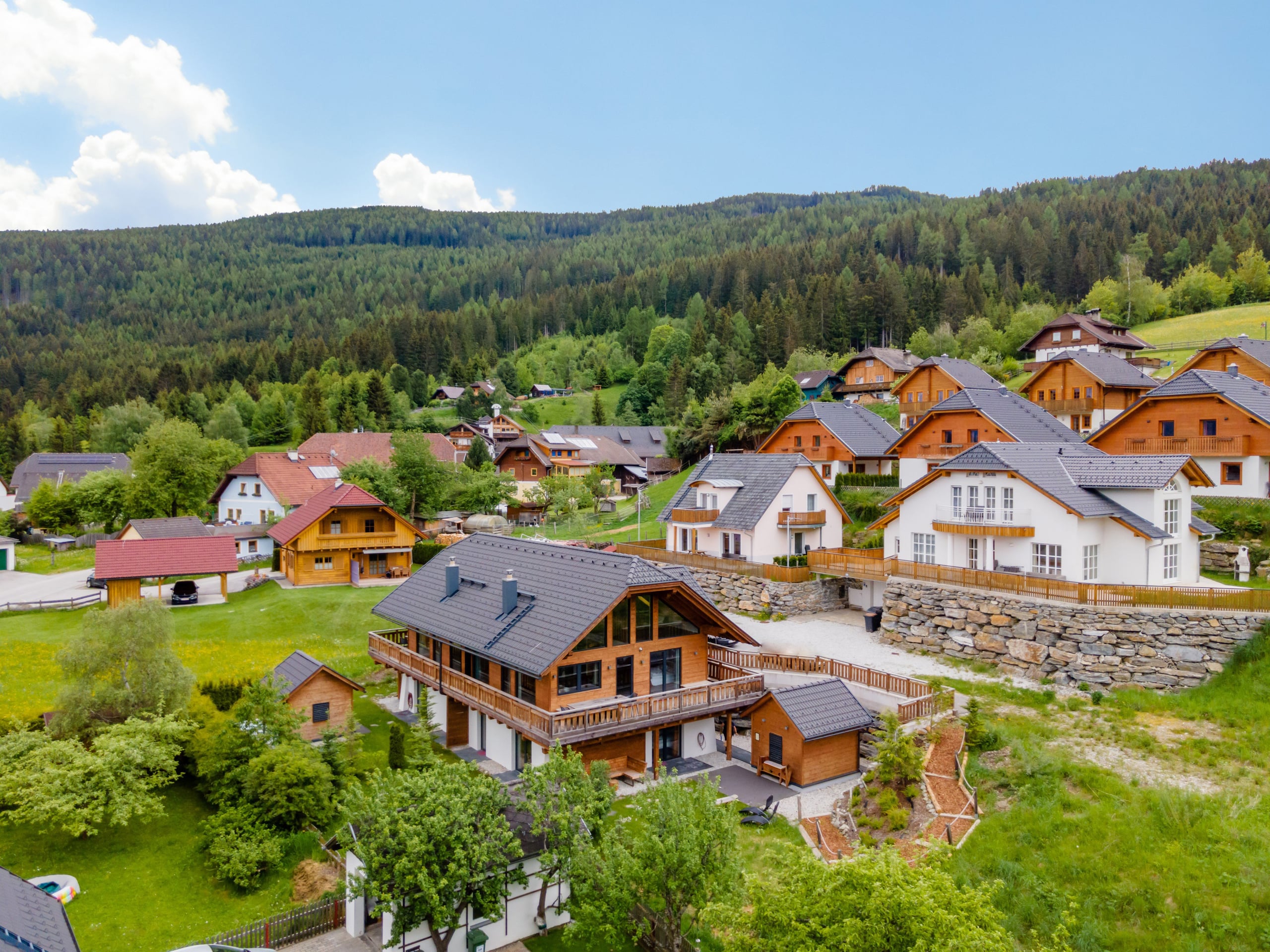 AlpInn Chalet zwischen den Häusern des Dorfes, mit Wäldern im Hintergrund