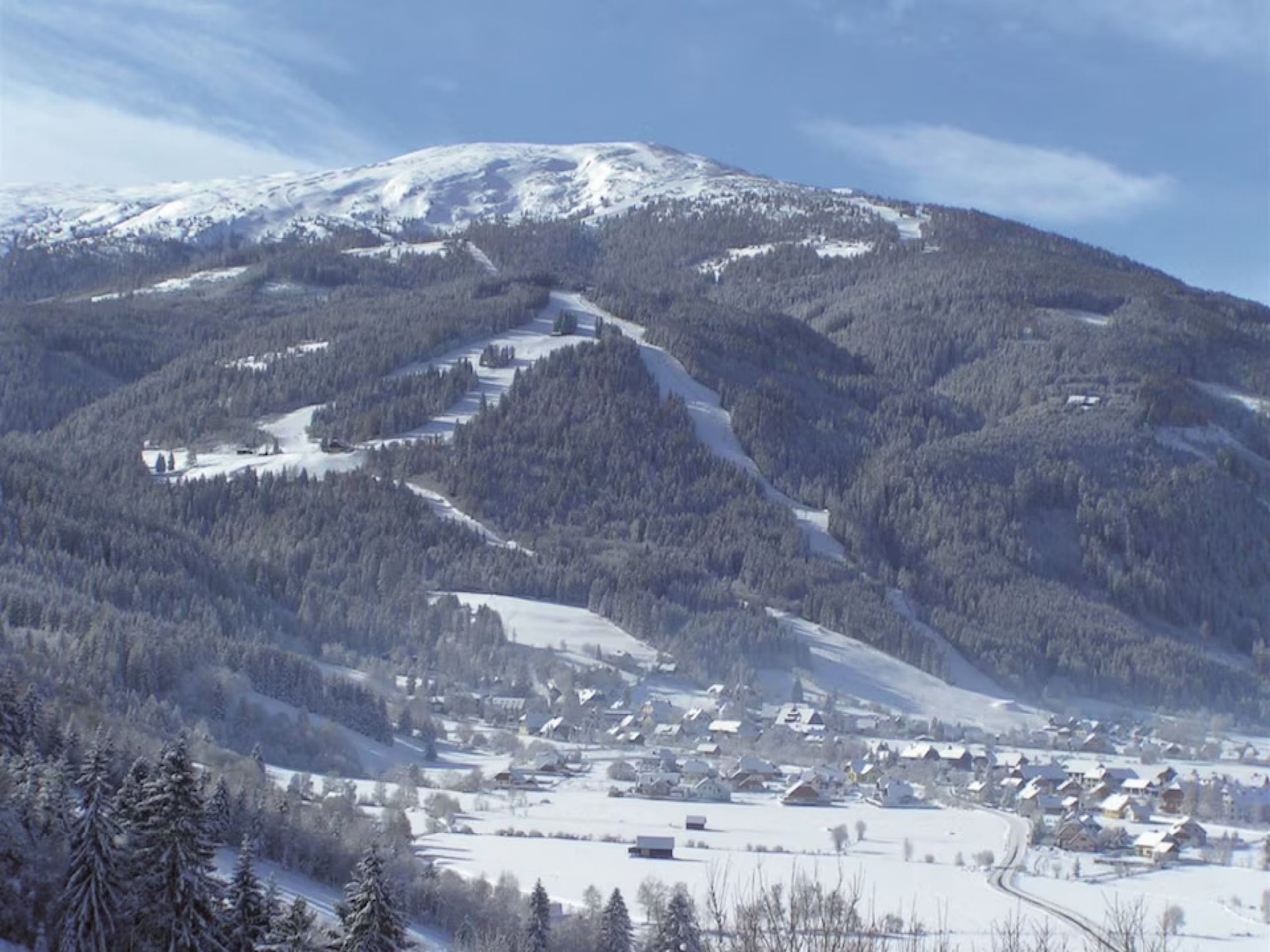 Snowy mountain with ski runs through the forest above the valley in the Salzburger Lungau